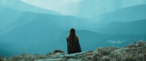 silhouette of a person sitting on a hill facing the mountains behind them